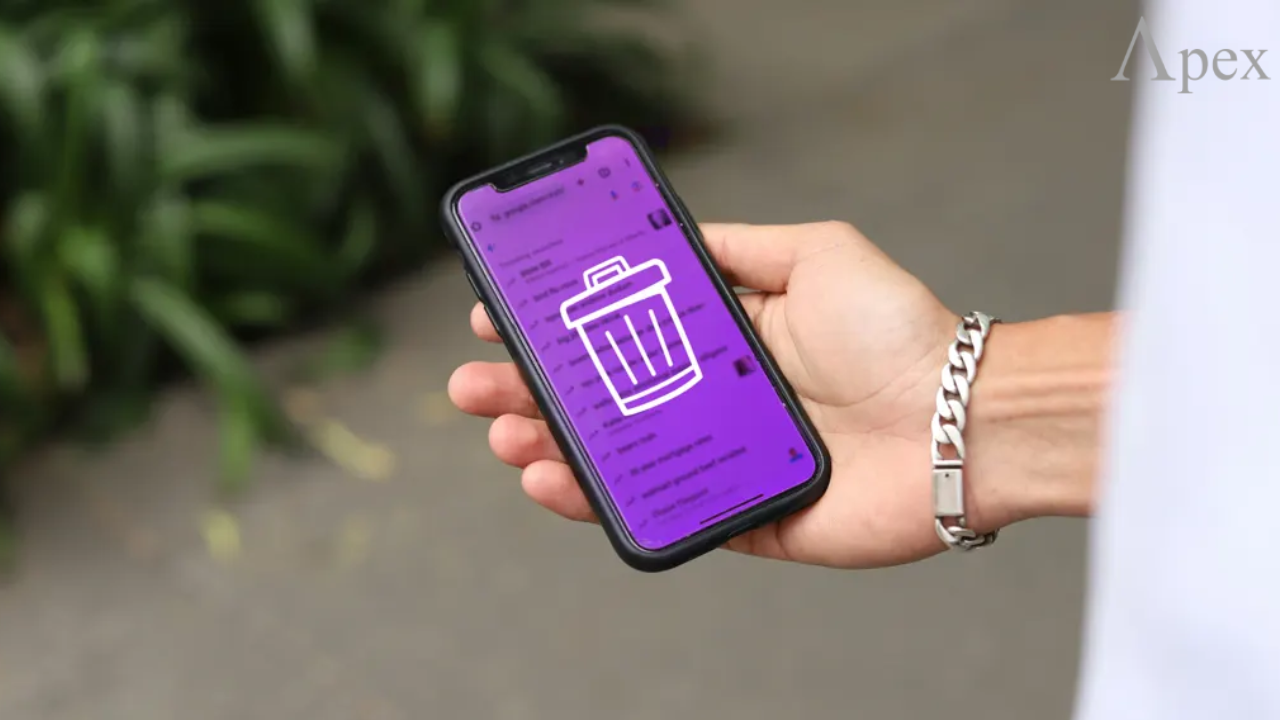 Person holding a smartphone with a trash bin icon on the screen, symbolizing deleting data or apps.