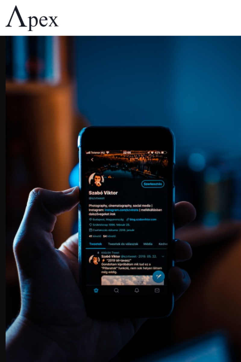 Hand holding a smartphone displaying a Twitter profile in dark mode at night