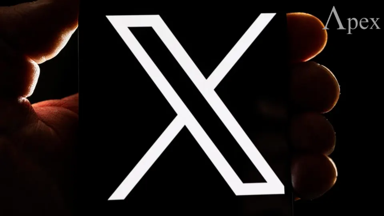 Close-up of a hand holding a phone displaying the white X logo on a black background.