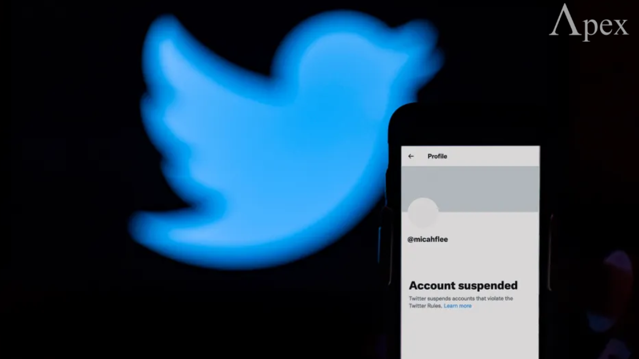 Phone screen showing a suspended Twitter account with the large Twitter bird logo in the background.